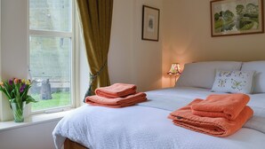 A neatly made bed with folded towels, a window with curtains, a vase of flowers, and a lamp on the bedside table. - 2 bedroom accommodation in Brancepeth, near Durham (Brancepeth, near Durham)