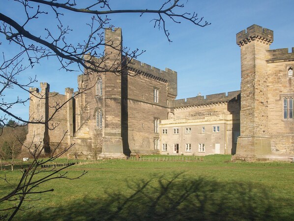A historic castle with a large central tower, multiple smaller towers, and a well-maintained lawn in front.