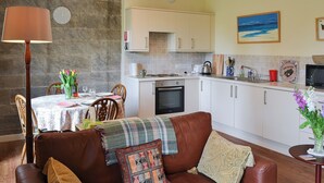 A cozy living room with a brown leather sofa, a dining table with chairs, and a kitchen area with white cabinets and a stove. - 2 bedroom accommodation in Brancepeth, near Durham (Brancepeth, near Durham)