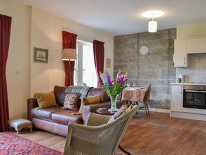 A cozy living room with a sofa, a wicker chair, a dining table with chairs, and a kitchen area with cabinets and a stove.