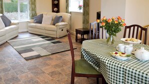 Ein Wohnzimmer mit einer Couch, einem Esstisch mit kariertem Tischläufer und einer Blumenvase.