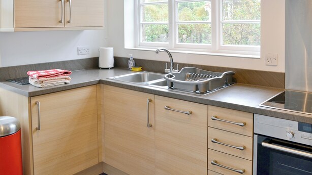 A modern kitchen with a stainless steel sink, wooden cabinets, and a window providing natural light.
