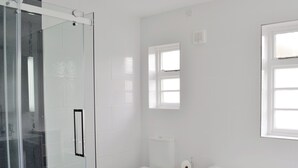 A bathroom with a glass shower enclosure, a toilet, a bathtub, and a window providing natural light.