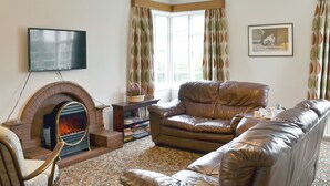 A living room with a fireplace, leather sofa, and a television mounted on the wall.