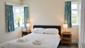 A neatly made bed with white linens and pillows, two bedside tables with lamps, and blue curtains with a leaf pattern.