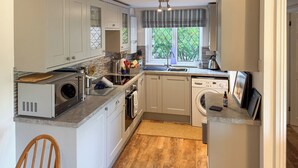 Una cocina compacta con electrodomésticos integrados, una ventana con cortinas y suelo de madera.
