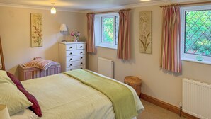 Un dormitorio con cama, cómoda, ventana con cortinas y radiador.