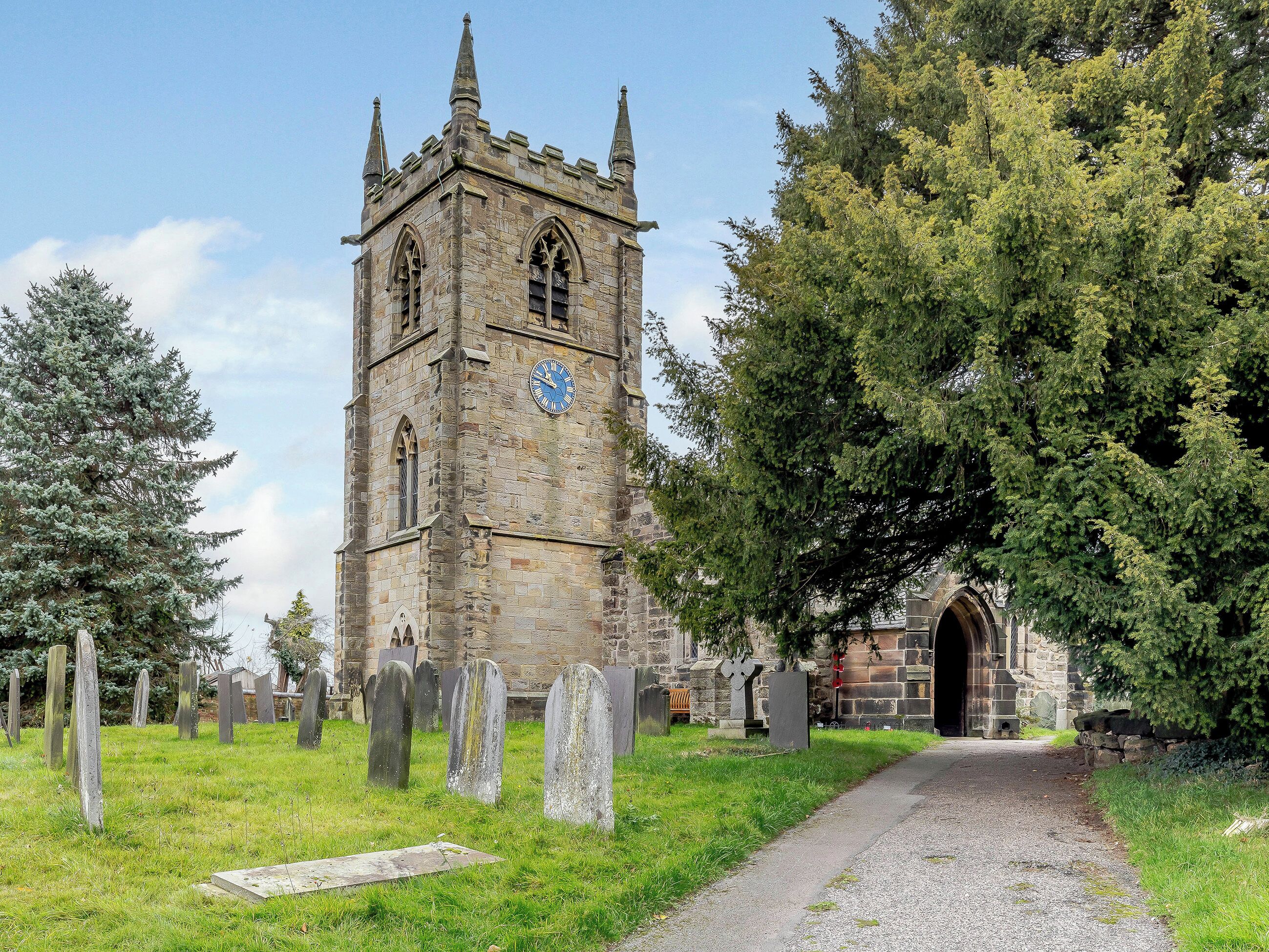 A church with a clock tower, graveyard, and a stone building with an arched entrance.