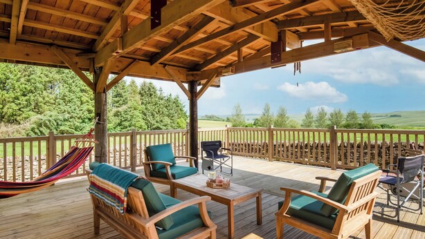 Una terraza de madera con mobiliario exterior, una hamaca y vistas al campo.
