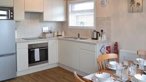 Une cuisine moderne avec des meubles blancs, un four encastré et un coin repas aménagé pour quatre personnes, comprenant une table, des chaises et de la vaisselle.