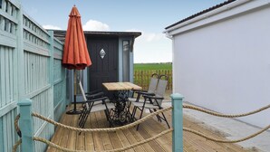 Une terrasse en bois avec une table et des chaises, une porte ornée d’un emblème en métal et une barrière faite de cordes.