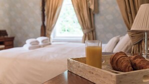 Une chambre à coucher avec un lit, une table de chevet sur laquelle se trouve une assiette de croissants et un verre de jus d’orange, et une fenêtre avec des rideaux.
