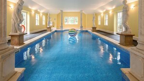 Une grande piscine intérieure, flanquée de statues de chaque côté, avec un ballon coloré et un mur jaune doté de fenêtres.