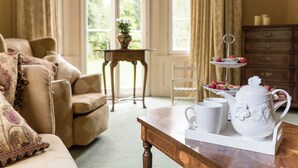 Un salon chaleureux avec un canapé, une table basse en bois sur laquelle sont posés une théière et des tasses, et un présentoir à gâteaux à trois niveaux.