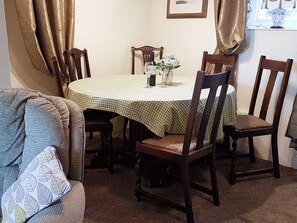 Een eetgedeelte met een ronde tafel, bedekt met een groen geruit tafelkleed, omringd door houten stoelen.