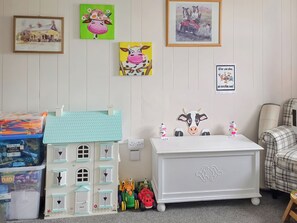 Een kinderspeelkamer met een poppenhuis, een witte dressoir en diverse speelgoed.