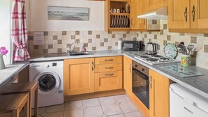 A compact kitchen with wooden cabinets, a washing machine, a microwave, and a coffee maker. - 3 bedroom accommodation in Aberdaron, Lleyn Peninsula (Aberdaron, Lleyn Peninsula)