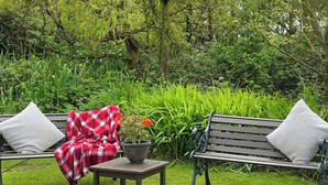 A garden with two wooden benches, a small table, and a potted plant. - 3 bedroom accommodation in Aberdaron, Lleyn Peninsula (Aberdaron, Lleyn Peninsula)