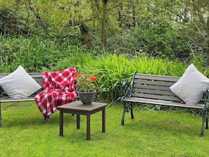 A garden with two wooden benches, a small table, and a potted plant. - 3 bedroom accommodation in Aberdaron, Lleyn Peninsula (Aberdaron, Lleyn Peninsula)