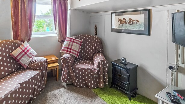A cozy room with a polka-dotted sofa, a small wooden table, a vintage stove, and a television. - 3 bedroom accommodation in Aberdaron, Lleyn Peninsula (Aberdaron, Lleyn Peninsula)