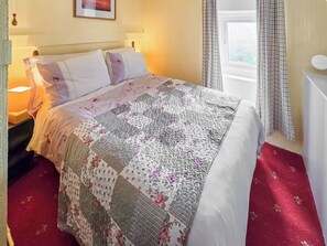 Een netjes opgemaakt bed met een quilt met bloemenprint, een bedlampje en een raam met gordijnen.