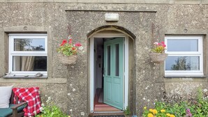 A stone building with a green door, potted plants, and a bench with a red and white checkered blanket. - 3 bedroom accommodation in Aberdaron, Lleyn Peninsula (Aberdaron, Lleyn Peninsula)