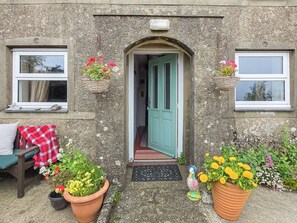 A stone building with a green door, potted plants, and a bench with a red and white checkered blanket. - 3 bedroom accommodation in Aberdaron, Lleyn Peninsula (Aberdaron, Lleyn Peninsula)