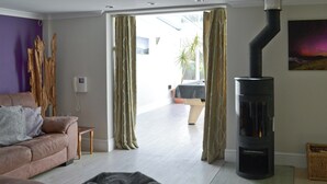 A living room with a sofa, a black ottoman, a fireplace, and a view through a doorway to an outdoor area. - 3 bedroom accommodation in Bude (Bude)