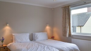 A bedroom with a double bed, bedside tables, a window with curtains, and a radiator. - 3 bedroom accommodation in Bude (Bude)