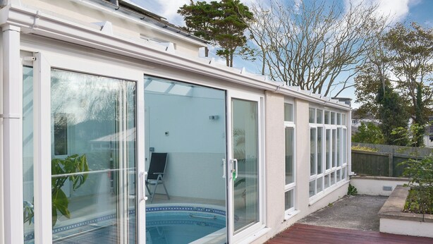 A modern house with a glass-enclosed swimming pool, a wooden deck, and a garden area. - 3 bedroom accommodation in Bude (Bude)