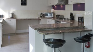A modern kitchen with a central island, white cabinets, a microwave, a toaster, and a sink. - 3 bedroom accommodation in Bude (Bude)