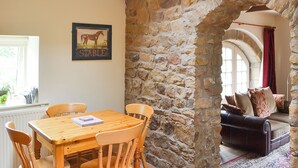 A dining area with a wooden table and chairs, a stone wall, and a cozy seating area with a sofa and cushions.