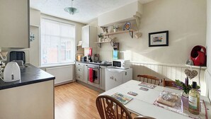 A compact kitchen with a dining table, wooden chairs, and a window with blinds.