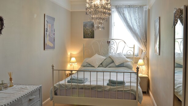 A bedroom with a bed, bedside tables, a dresser, a chandelier, and artwork on the walls.