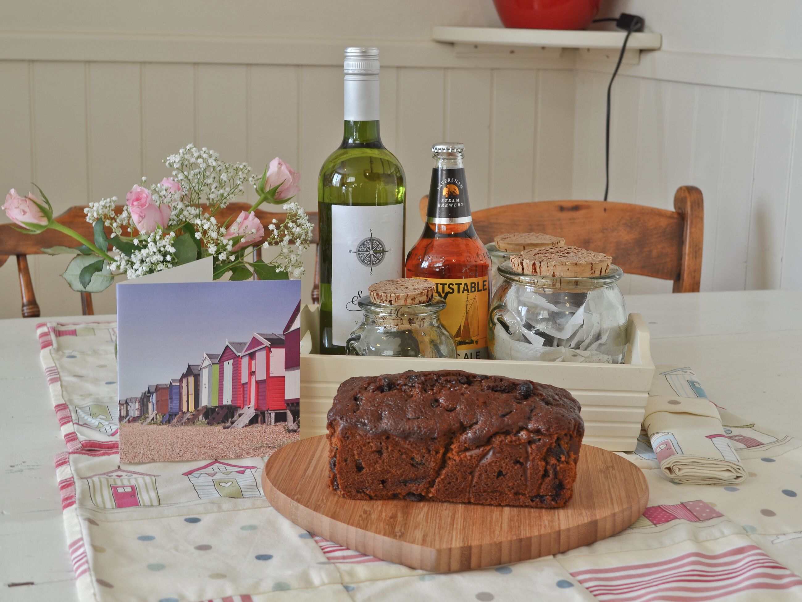 Une table avec un pain, une bouteille de vin, un bocal de biscuits, une carte et un vase de fleurs.