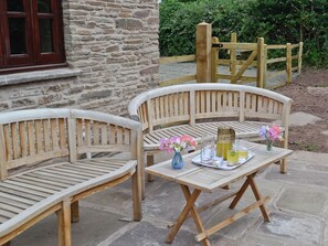 Two wooden benches with a table between them, a vase with flowers, and a tray with drinks and glasses.