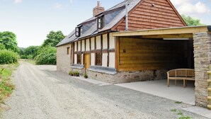 Une maison traditionnelle en pierre avec une extension en bois, une allée en gravier et un banc à l’extérieur.