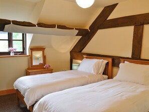 Een slaapkamer met twee enkele bedden, houten balken, een raam met uitzicht, een nachtkastje met spiegel en een vaas met bloemen.