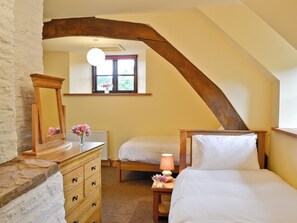 Un dormitorio con una cama de madera, un aparador, una mesita de noche con lámpara y una ventana con vistas a la vegetación.