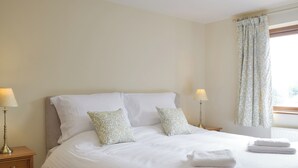A neatly made bed with white linens and two decorative pillows, a bedside lamp, and a window with a curtain. - Woodpecker Cottage - UKC3412 (Bolton-by-Bowland)