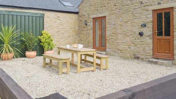 A stone building with a wooden table and benches, a green door, and potted plants. - Woodpecker Cottage - UKC3412 (Bolton-by-Bowland)