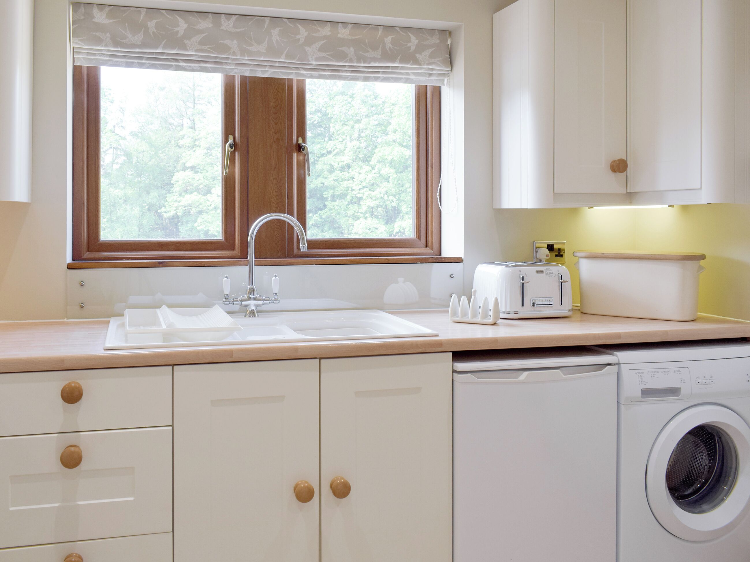 A kitchen with a sink, a toaster, a washing machine, and cabinets.
