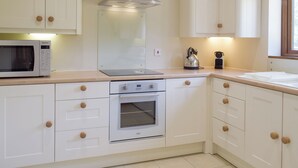 A modern kitchen with white cabinets, a stainless steel range hood, a microwave, an oven, and a kettle. - Woodpecker Cottage - UKC3412 (Bolton-by-Bowland)