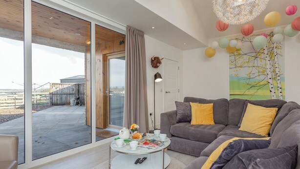 Een moderne woonkamer met een grijze bank, een bijzettafeltje en een grote schuifdeur naar een buitenruimte.