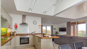 Een moderne keuken met een centraal eiland, een eetgedeelte met een tafel voor twee personen, en een zithoek met een bank.