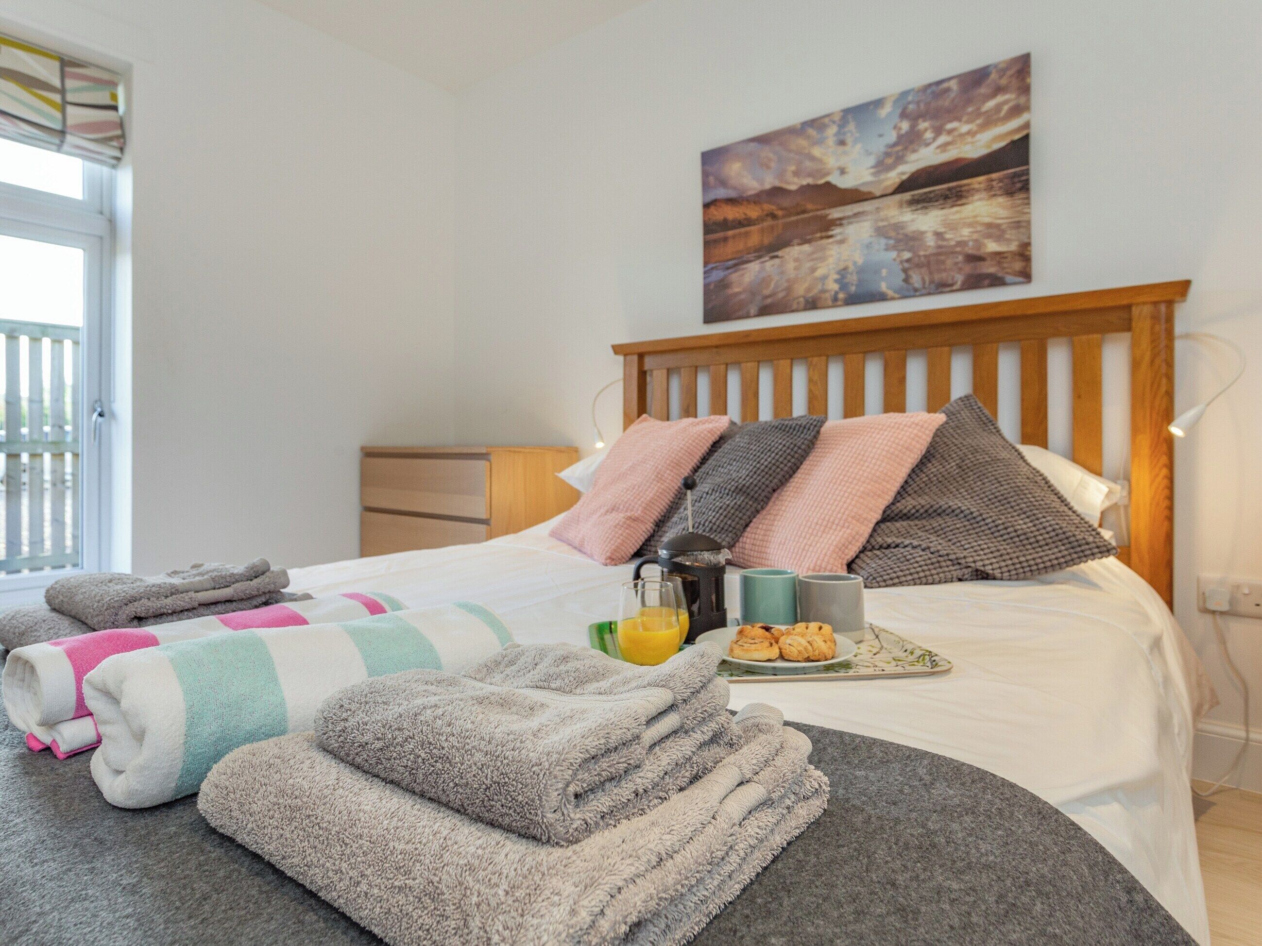 Een keurig opgemaakt bed met houten hoofdbord, een nachtkastje met een lamp, en een schilderij aan de muur.