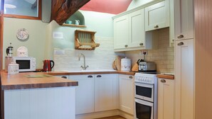 Una cocina con armarios blancos, encimera de madera, fregadero, estufa y microondas.