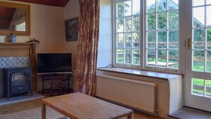 Una sala de estar acogedora con chimenea, televisor, banca de mimbre y un ventanal con vistas al jardín.
