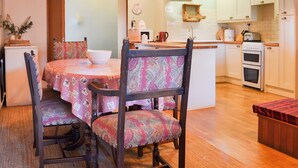 Una cocina acogedora con vigas de madera, una mesa de comedor con sillas estampadas y armarios blancos.