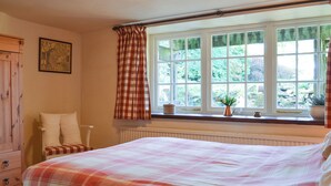 Un dormitorio con una cama grande, una ventana con cortinas, un radiador y un aparador de madera.